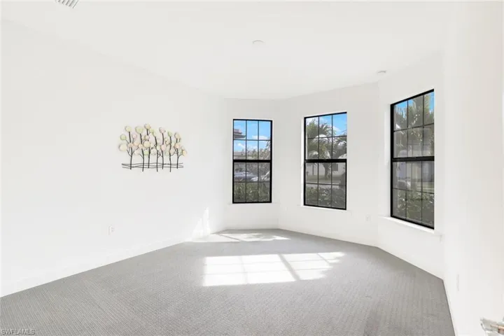 Bright interior room featuring a curved wall with three large grid-pattern windows, light gray carpet flooring, white baseboards, and recessed ceiling lighting