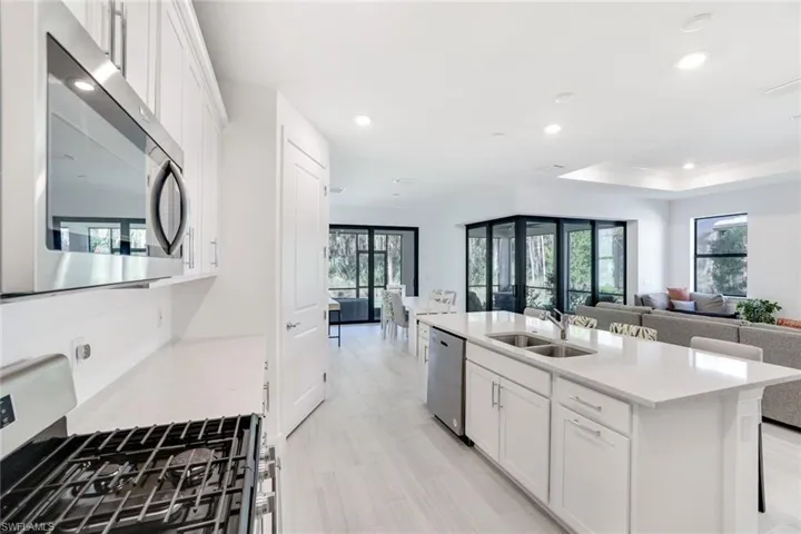 Open-concept kitchen featuring white cabinetry, stainless steel appliances, a center island with double sink, and light wood-finish flooring