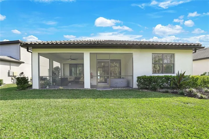 Expansive backyard featuring a manicured lawn, screened-in patio, and mature landscaping