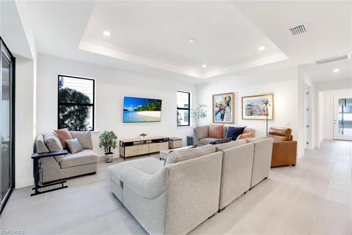 Spacious living area featuring light-toned tile flooring, tray ceiling with recessed lighting, and expansive sliding glass doors