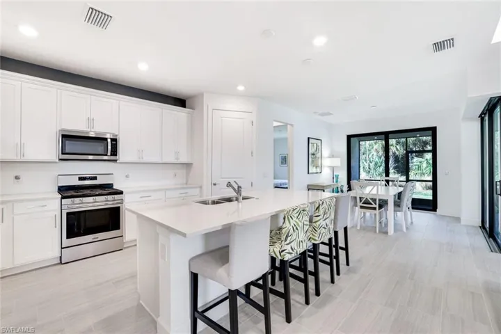 Bright kitchen featuring an island with integrated sink, white cabinetry, stainless steel appliances, and a dining area with sliding glass doors