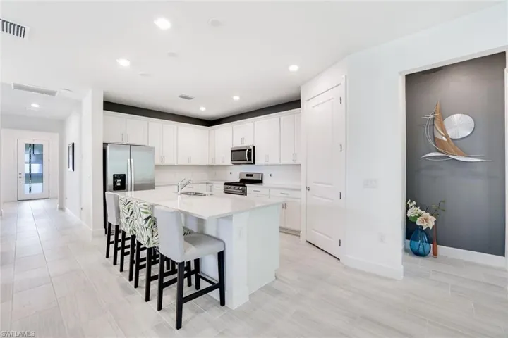 Kitchen featuring white cabinetry, stainless steel appliances, a white island with seating, and light-toned tile flooring
