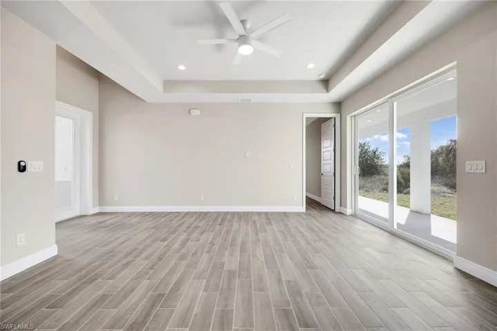 Empty room with wood finish floors, a ceiling fan, a tray ceiling, and recessed lighting-Finishes may vary