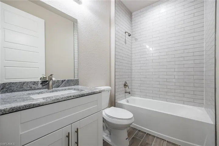 Bathroom with wood finish floors, shower / washtub combination, vanity, and a textured wall-Finishes may vary