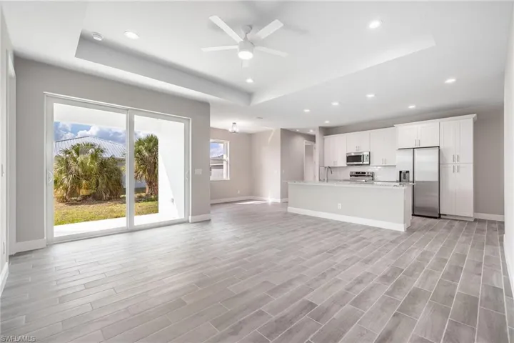 Unfurnished living room featuring ceiling fan, a raised ceiling, recessed lighting, and wood tiled floors-Finishes may vary