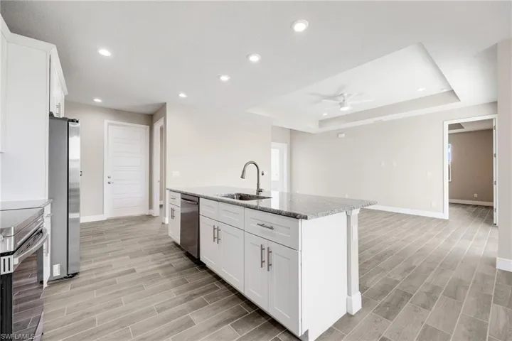 Kitchen featuring white cabinetry, light stone countertops, wood finish floors, recessed lighting, and appliances with stainless steel finishes-Finishes may vary