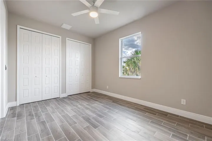 Unfurnished bedroom with two closets, wood tiled floors, and ceiling fan-Finishes may vary