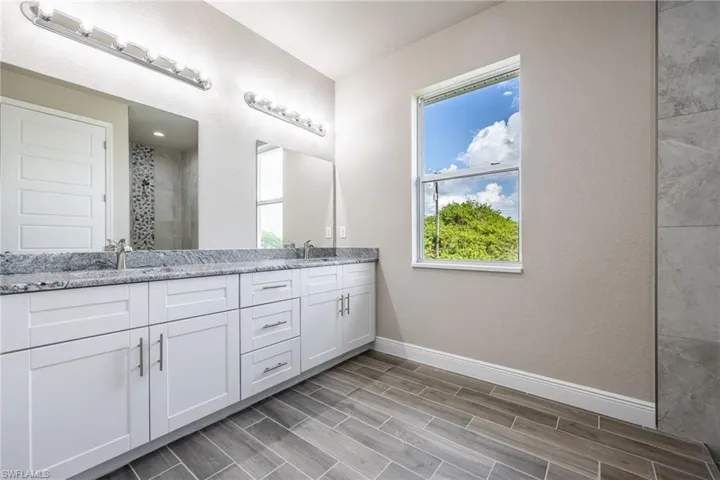 Bathroom with double vanity, a stall shower, wood finish floors, and a textured wall-Finishes may vary