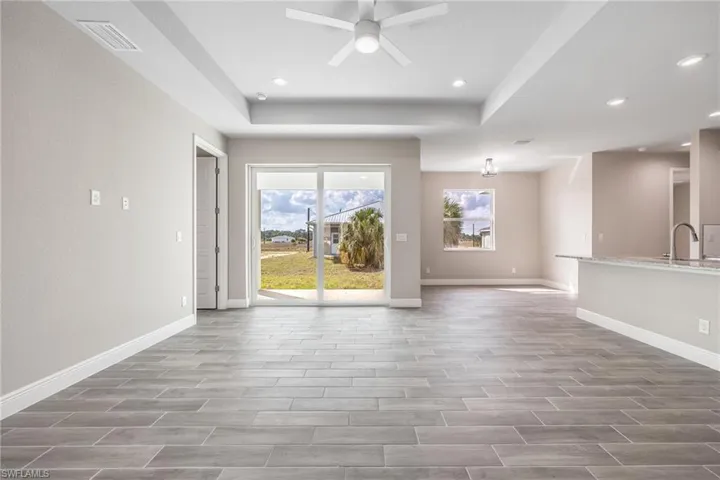 Unfurnished living room featuring ceiling fan, wood finish floors, a tray ceiling, and recessed lighting-Finishes may vary