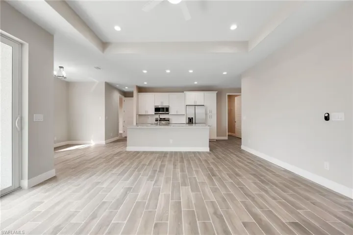 Unfurnished living room featuring recessed lighting, wood finish floors, ceiling fan, and a tray ceiling-Finishes may vary