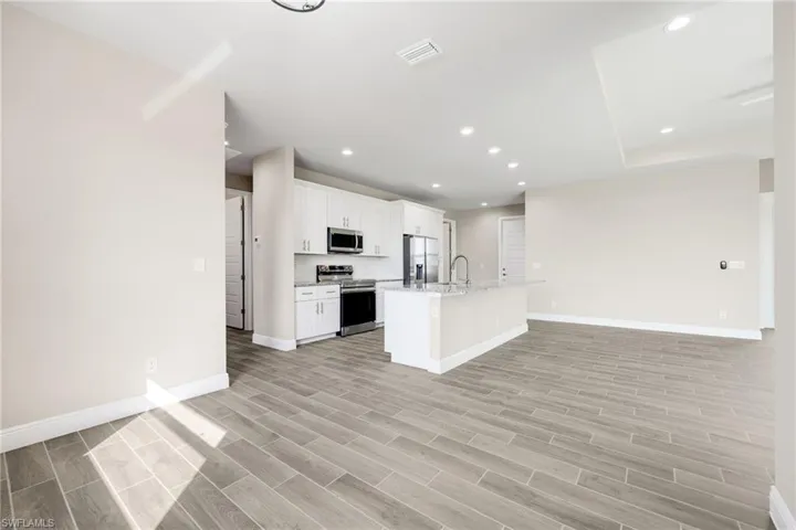 Kitchen with open floor plan, a kitchen island with sink, stainless steel appliances, recessed lighting, and white cabinetry-Finishes may vary