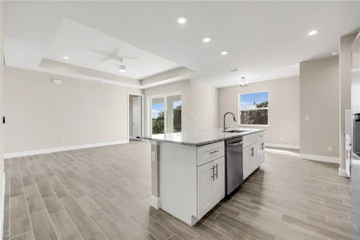 Kitchen with wood finish floors, light stone counters, open floor plan, white cabinets, and an island with sink-Finishes may vary