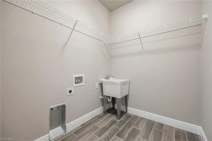 Laundry area featuring wood finish floors, hookup for a washing machine, hookup for an electric dryer, and a textured wall-Finishes may vary