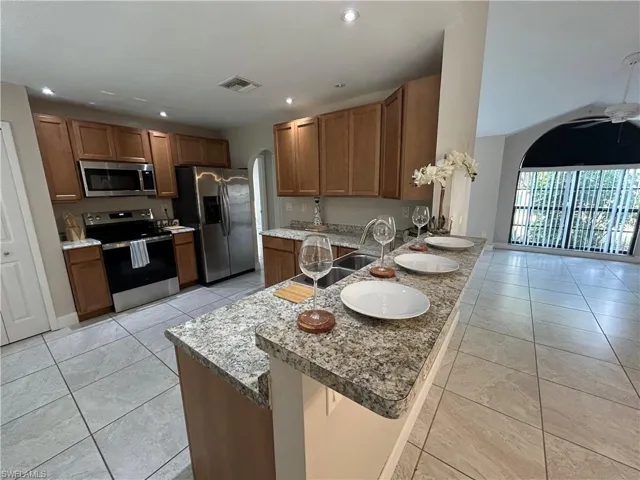 Kitchen featuring arched walkways, stainless steel appliances, wood finish cabinetry, a peninsula, and a kitchen bar