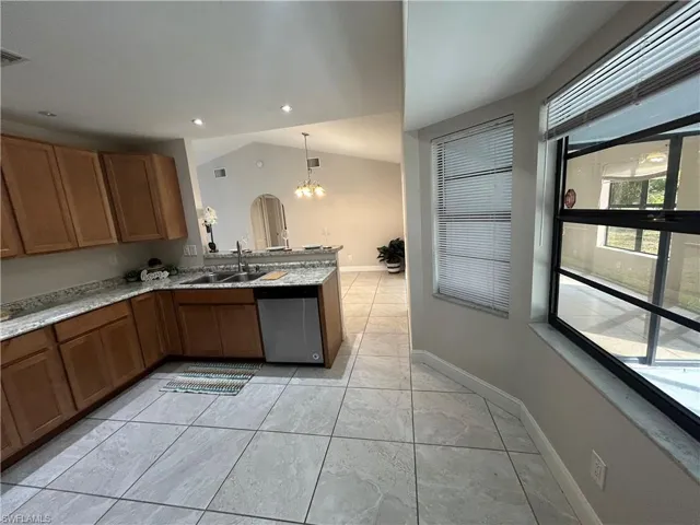 Kitchen featuring hanging lights, lofted ceiling, wood finish cabinetry, stainless steel dishwasher, and a peninsula
