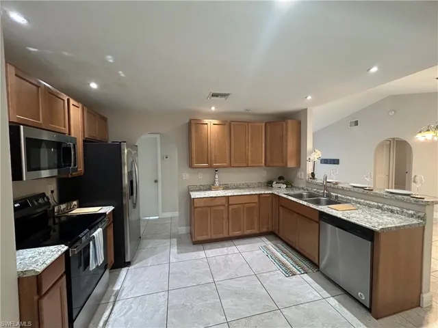Kitchen with arched walkways, stainless steel appliances, wood finish cabinetry, lofted ceiling, and recessed lighting