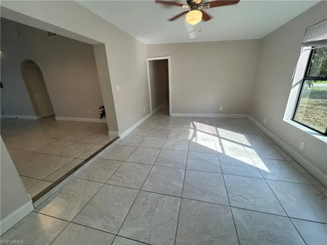 Empty room featuring arched walkways, ceiling fan, and light tile patterned floors