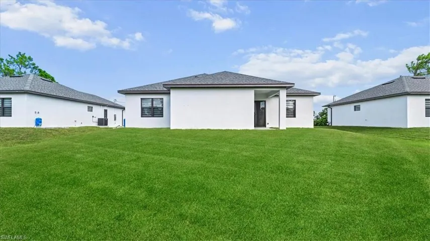 Rear view of property with a lawn, stucco siding, and a shingled roof