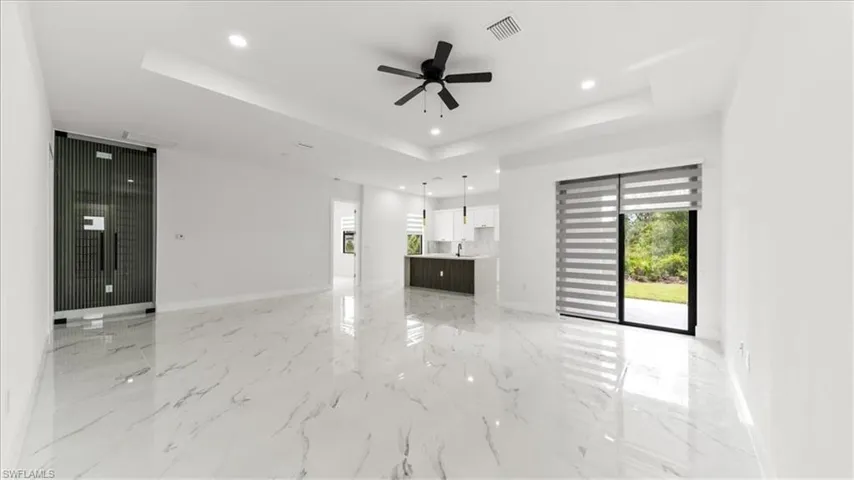 Unfurnished living room with a raised ceiling, recessed lighting, light marble finish flooring, and a ceiling fan