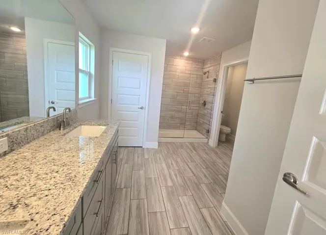 Bathroom featuring toilet, walk in shower, and vanity