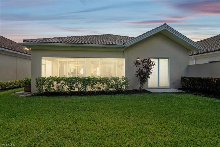 Back of house at dusk with a yard, stucco siding, and a tiled roof