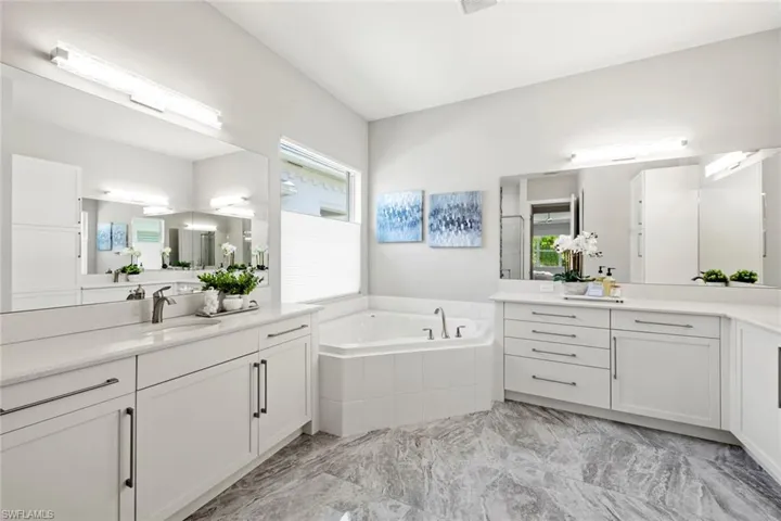 Primary en suite bathroom with large soaking tub, marble finish floor, dual sinks and vanities