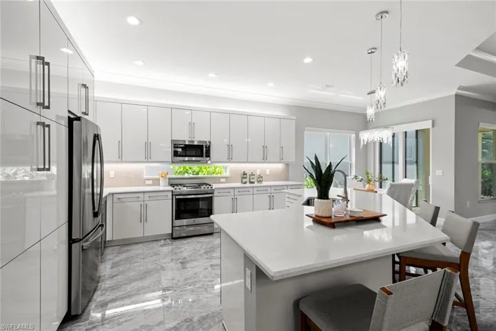 Light and bright kitchen featuring all Stainless steel GE appliances, quartz countertops, beautiful backsplash, built in wine cabinet, and picture window