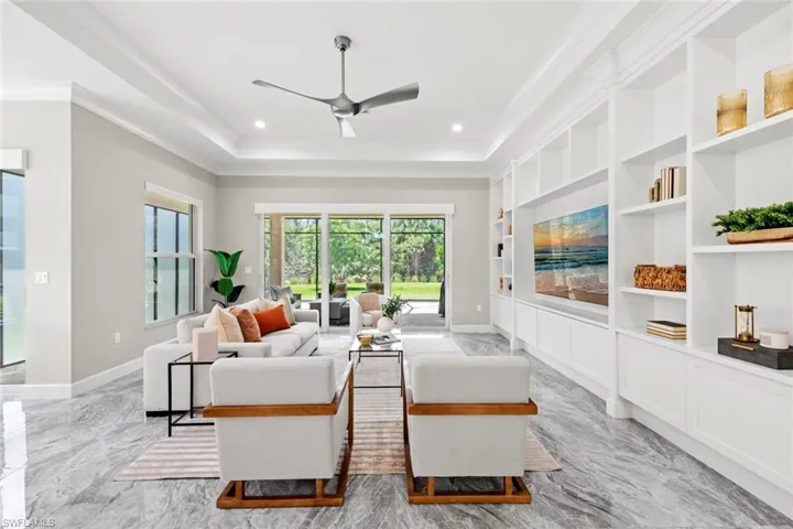 Living area featuring a tray ceiling, baseboards, ornamental molding, a ceiling fan, and custom built in entertainment center
