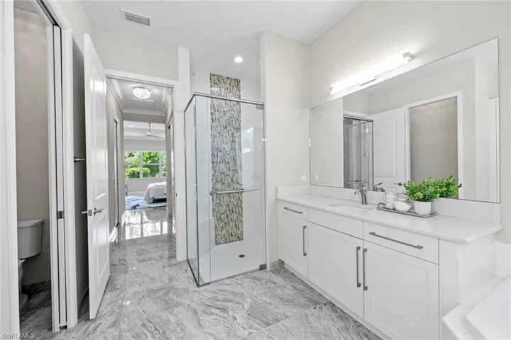 Ensuite bathroom featuring dual vanity, water closet, beautiful tile shower, marble finish floor