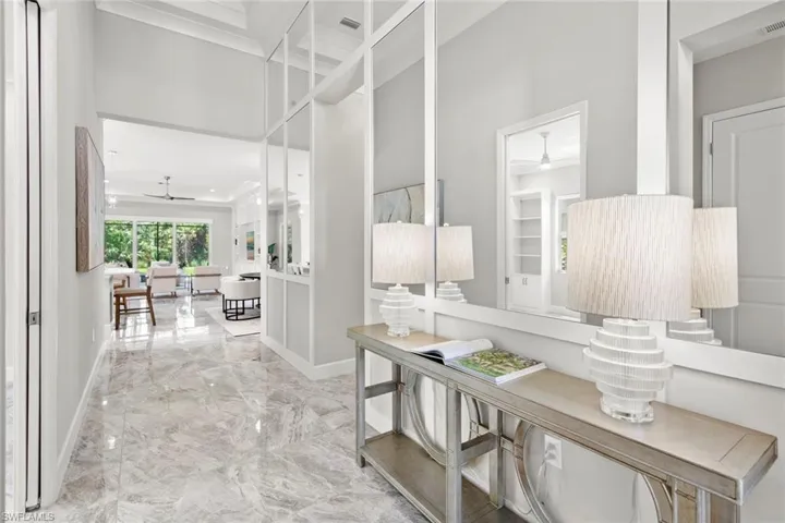 Corridor featuring crown molding, marble finish tile floor, and custom mirrored wall with chair-rail molding