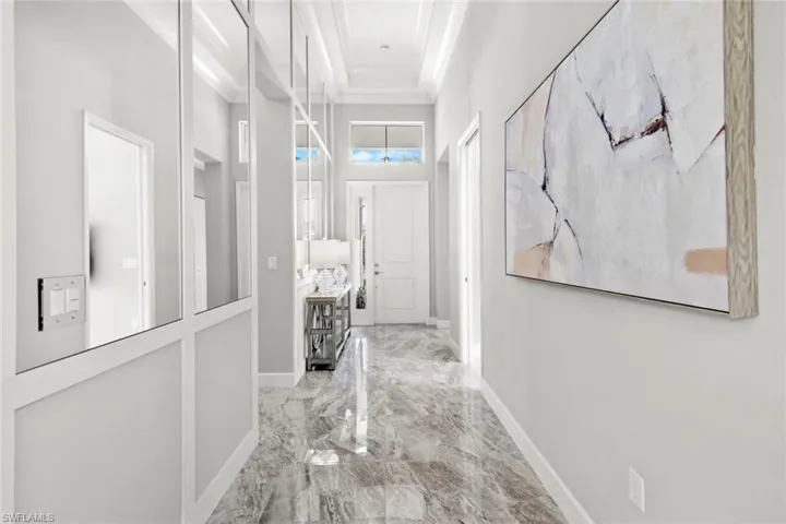 Corridor with ornamental molding, a towering ceiling, marble finish tile floor, and baseboards