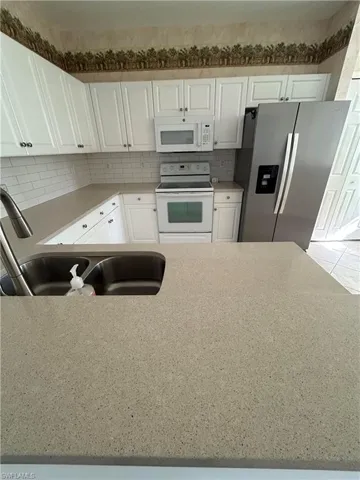 Kitchen featuring white appliances, white cabinetry, decorative backsplash, and light stone counters