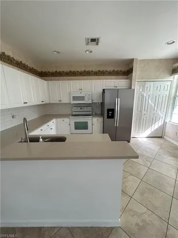 Kitchen featuring white appliances, white cabinets, a peninsula, light tile patterned flooring, and decorative backsplash