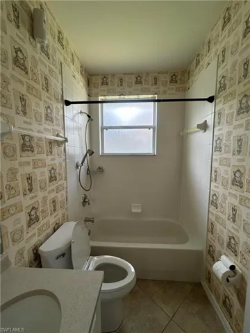 Bathroom featuring wallpapered walls, bathtub / shower combination, light tile patterned floors, and vanity