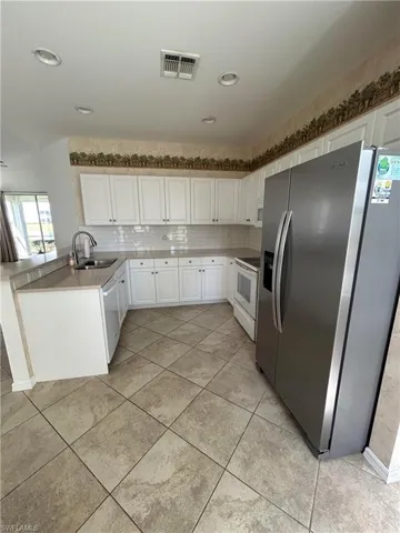 Kitchen with stainless steel appliances, white cabinets, a peninsula, light countertops, and backsplash