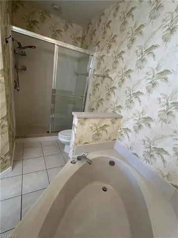 Bathroom with wallpapered walls, a bath, light tile patterned floors, and a stall shower