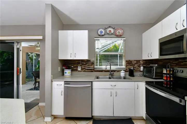 The kitchen features white cabinetry, a stainless steel dishwasher, and a window with blinds overlooking the outdoors