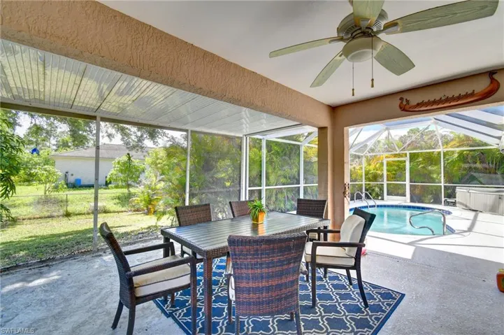 The screened-in patio features a ceiling fan, an outdoor dining table with chairs, and a pool area with a hot tub