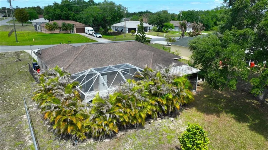 The property features a screened-in pool enclosure, a shingled roof, and an expansive yard with mature trees