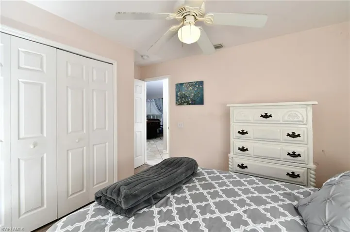 This room features light pink walls, a ceiling fan with a light fixture, and white bi-fold closet doors