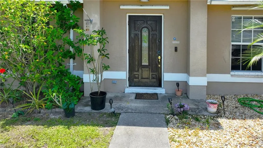 The property features a front entrance with a decorative dark wood door and an adjacent window with white muntins, set against a neutral-toned facade with white trim