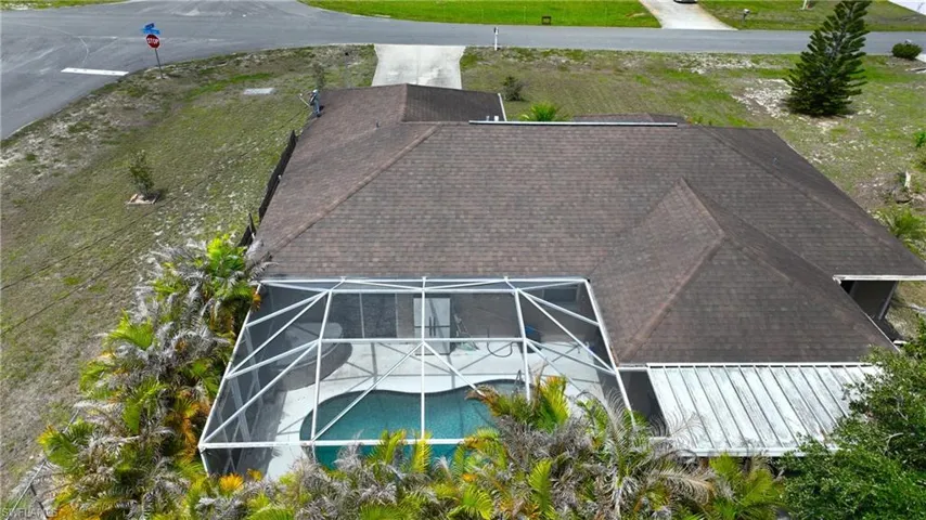 Property featuring a screened pool area, a brown shingle roof, and surrounding green landscaping