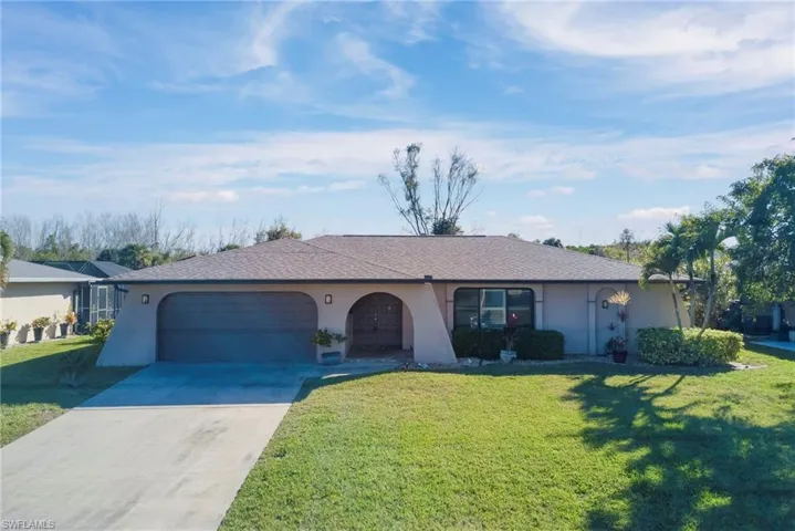 Ranch-style home featuring driveway, stucco siding, a front yard, an attached garage, and a shingled roof