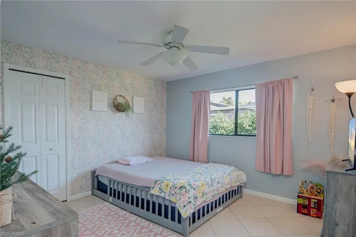 Bedroom featuring wallpapered walls, ceiling fan, light tile patterned floors, and a closet