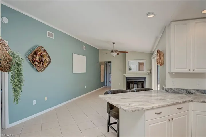 Kitchen with a breakfast bar, white cabinetry, a glass covered fireplace, a peninsula, and vaulted ceiling