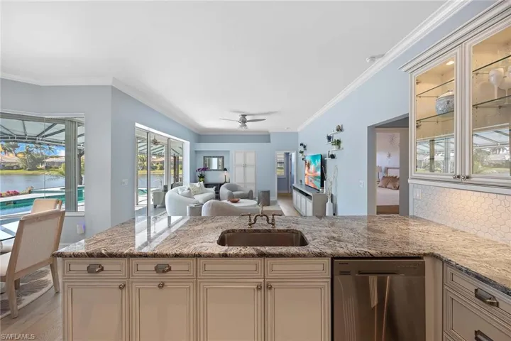 Kitchen with stainless steel dishwasher, light stone countertops, open floor plan, ornamental molding, and a peninsula