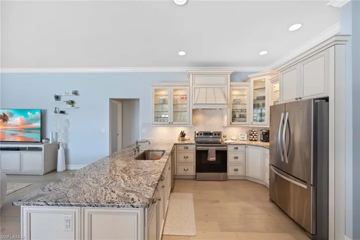 Kitchen featuring light stone countertops, stainless steel appliances, a peninsula, glass insert cabinets, and crown molding