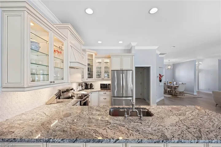 Kitchen with stainless steel appliances, ornamental molding, light stone counters, glass insert cabinets, and premium range hood