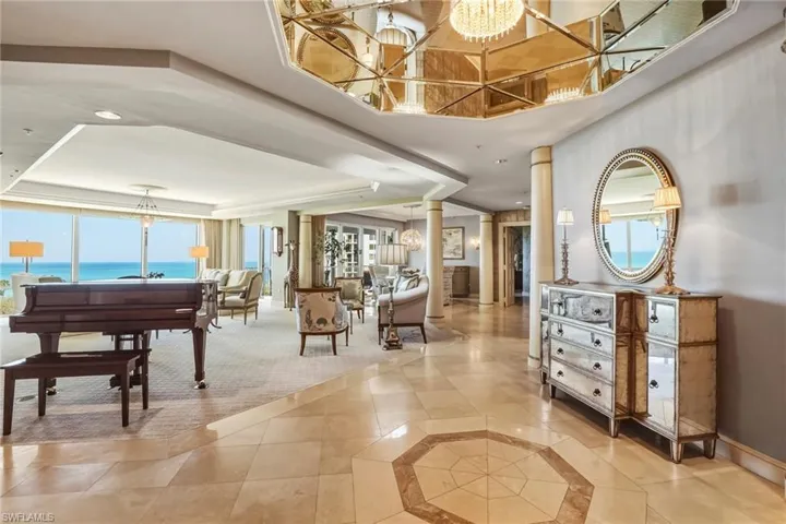 Foyer entrance with a chandelier, decorative columns, a raised ceiling, light tile patterned floors, and inlaid floor details
