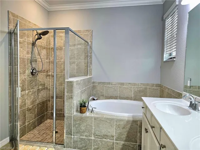 Bathroom featuring vanity, crown molding, and plus walk in shower